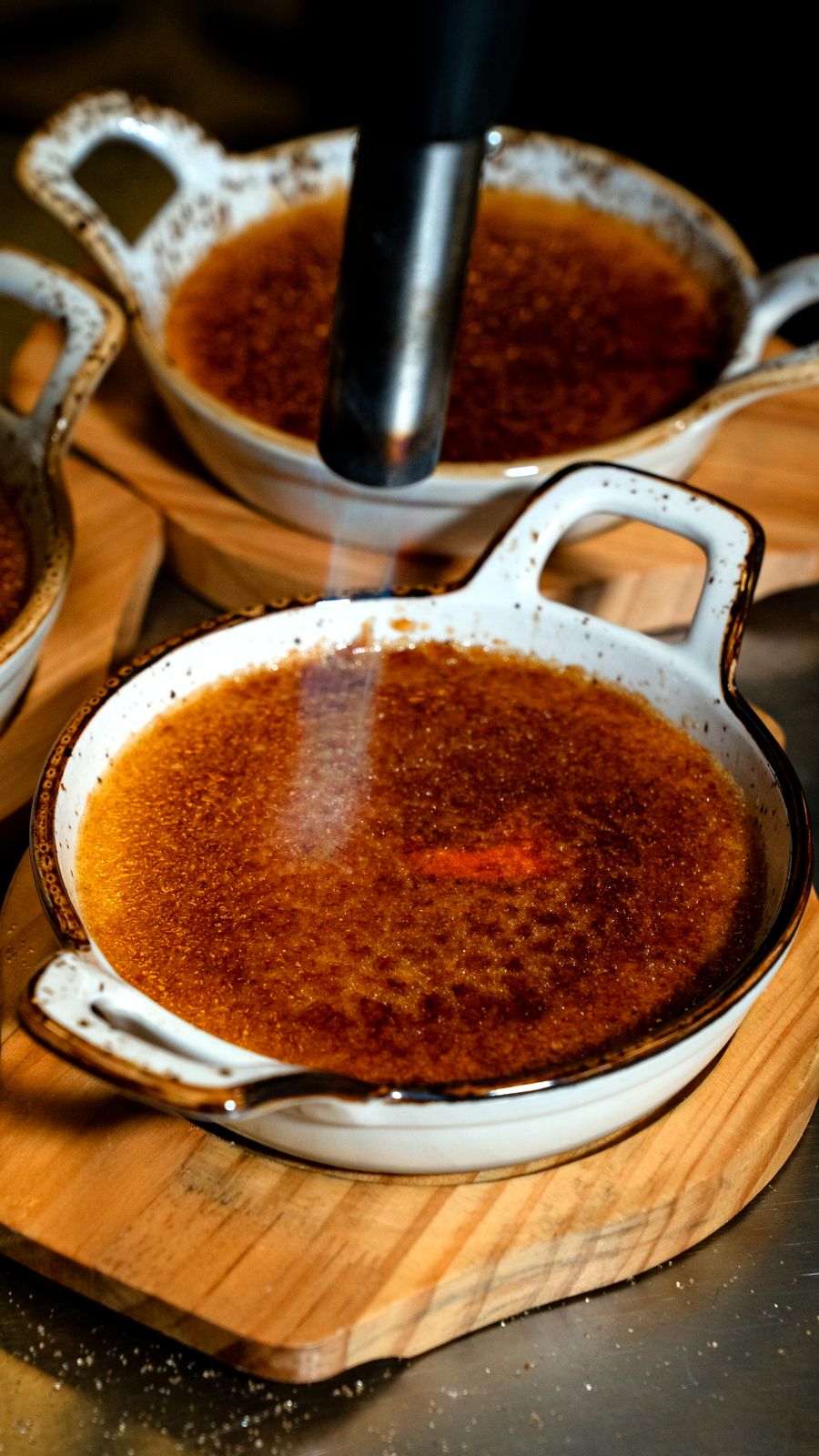 Creme brûlée sendo caramelizado com maçarico em tigela rústica