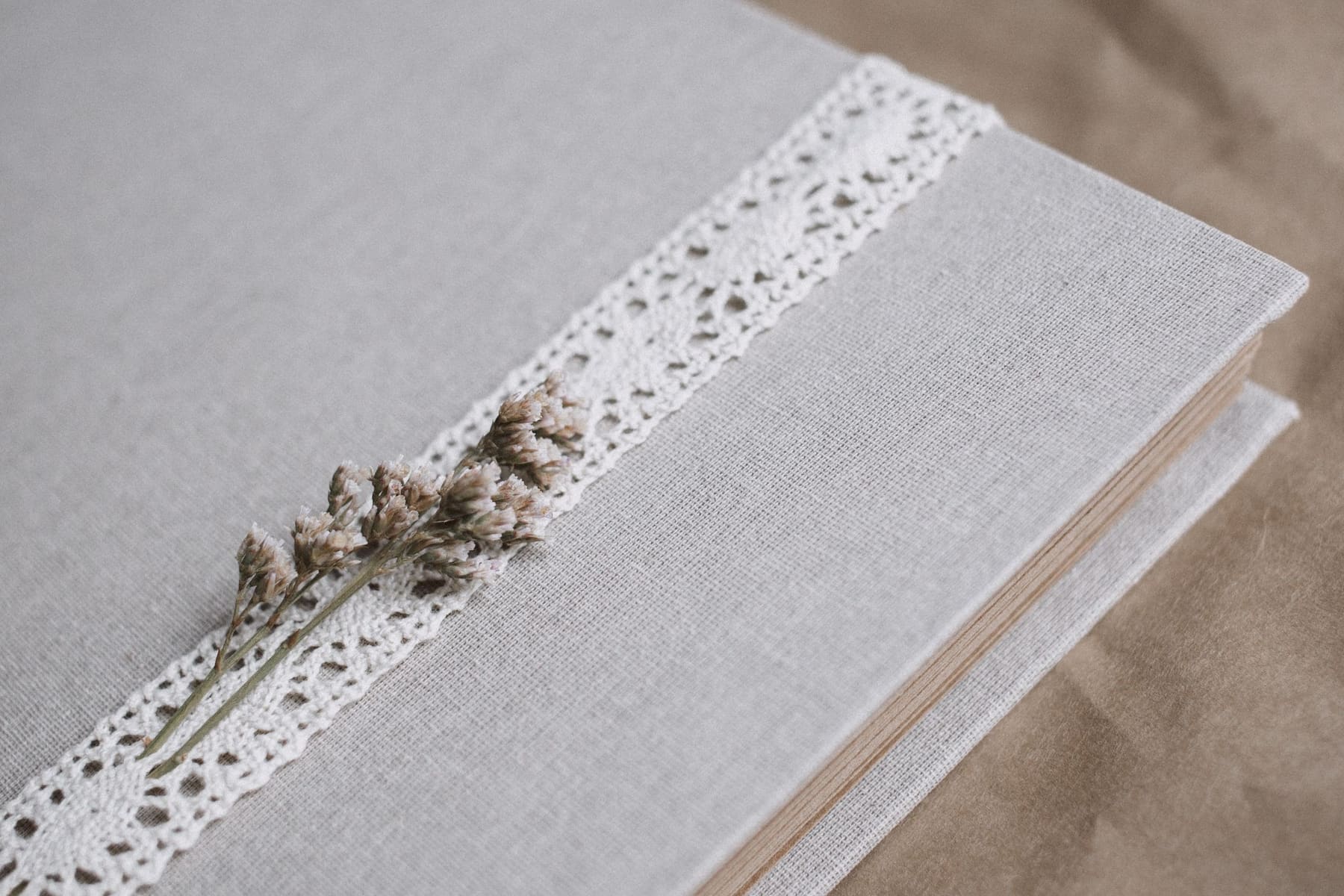 Um álbum de casamento fine-art de capa de linho, com detalhe de renda e flor seca, sobre a mesa.