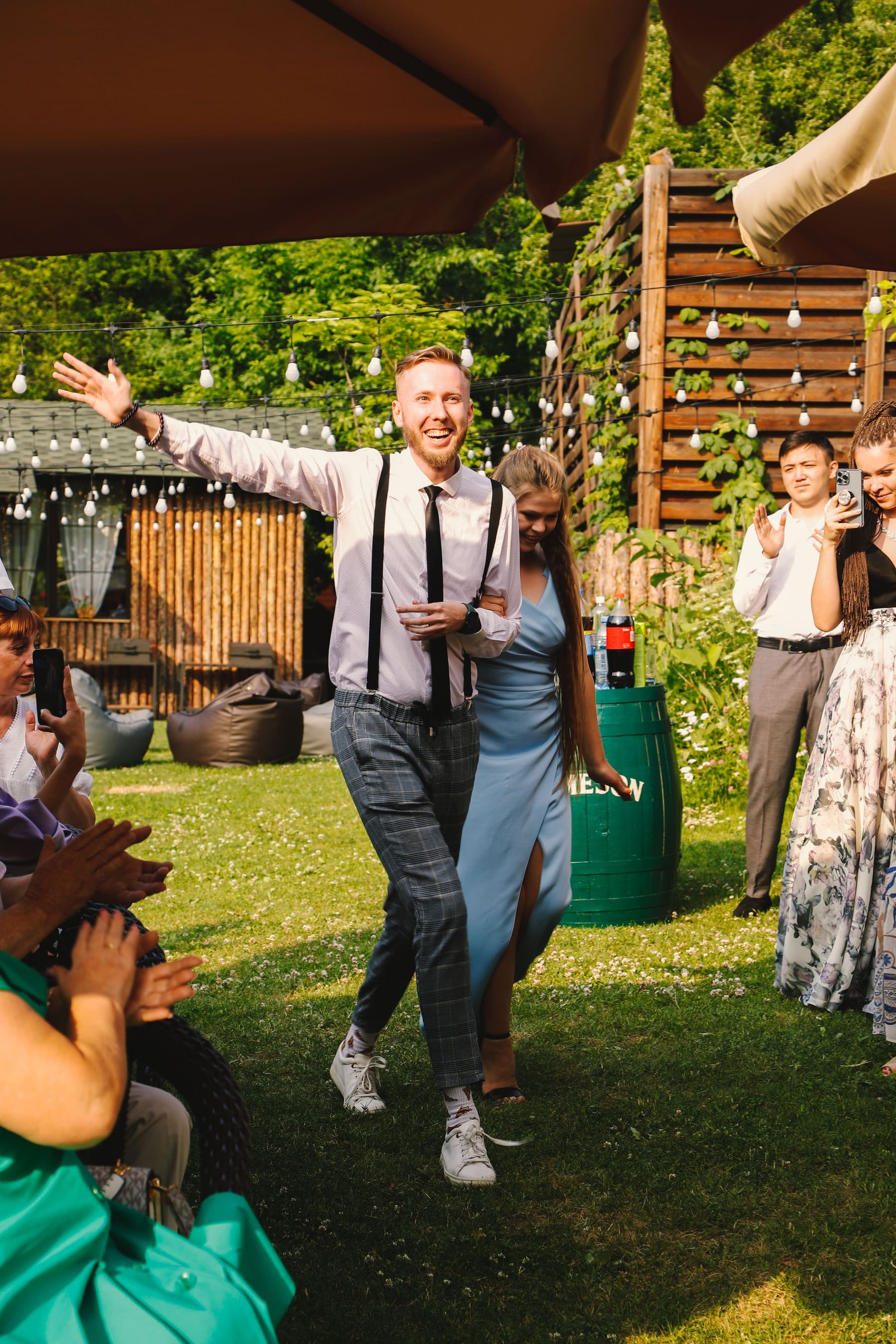 Um convidado sorrindo e comemorando, aplaudido por outros convidados, num instante espontâneo da festa.