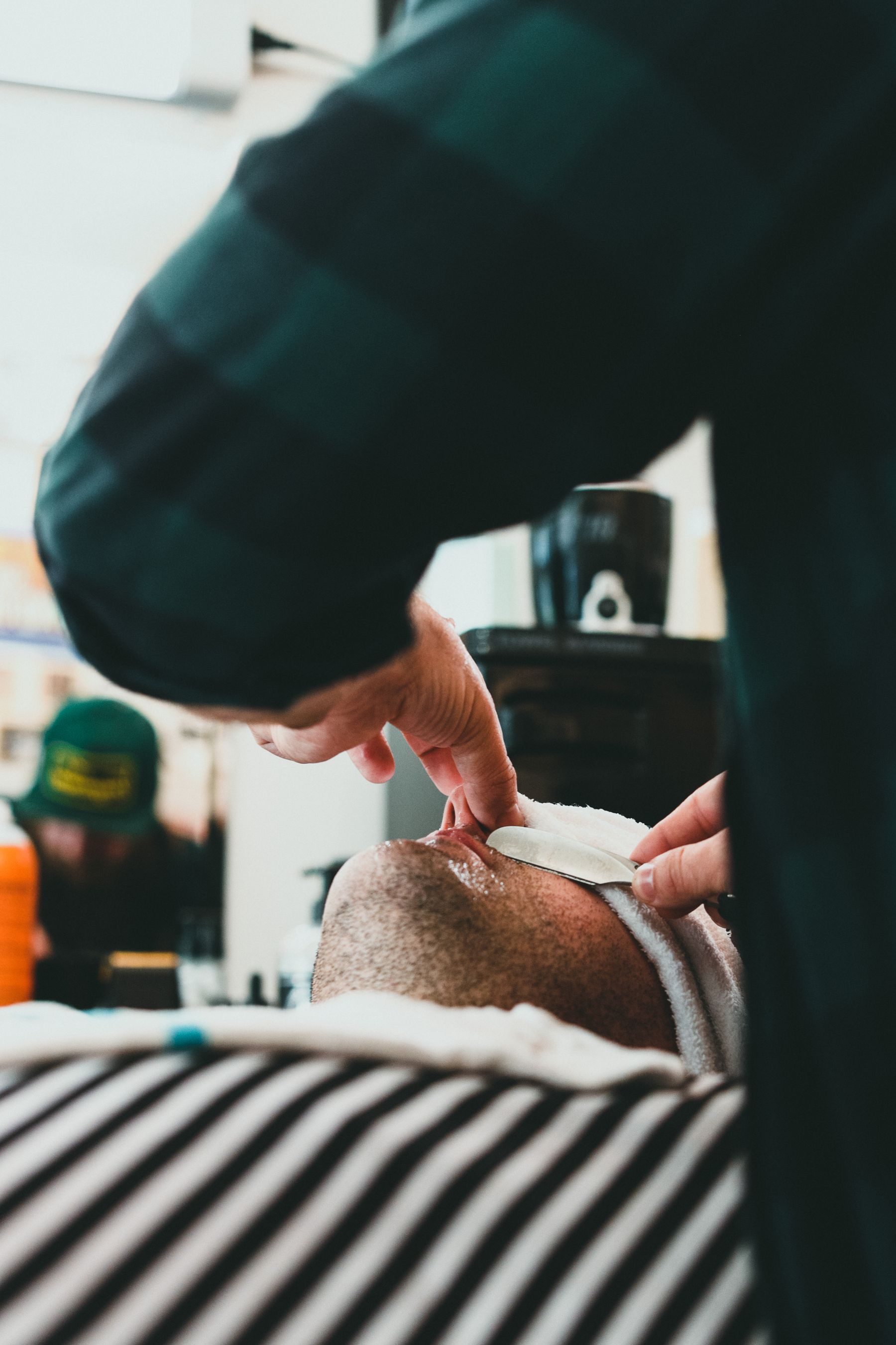 Barbeiro passando a navalha para alinhar a barba, com a toalha quente ao lado.